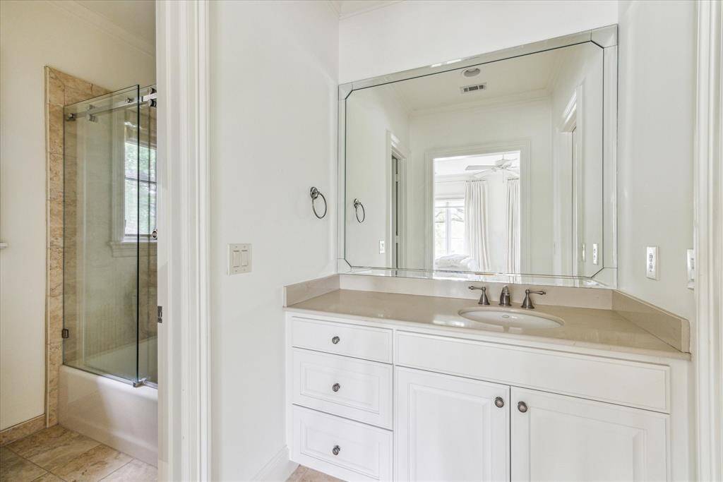 The bright ensuite bath features a large mirrored vanity, neutral stone countertop, and tub-shower combo with glass enclosure.