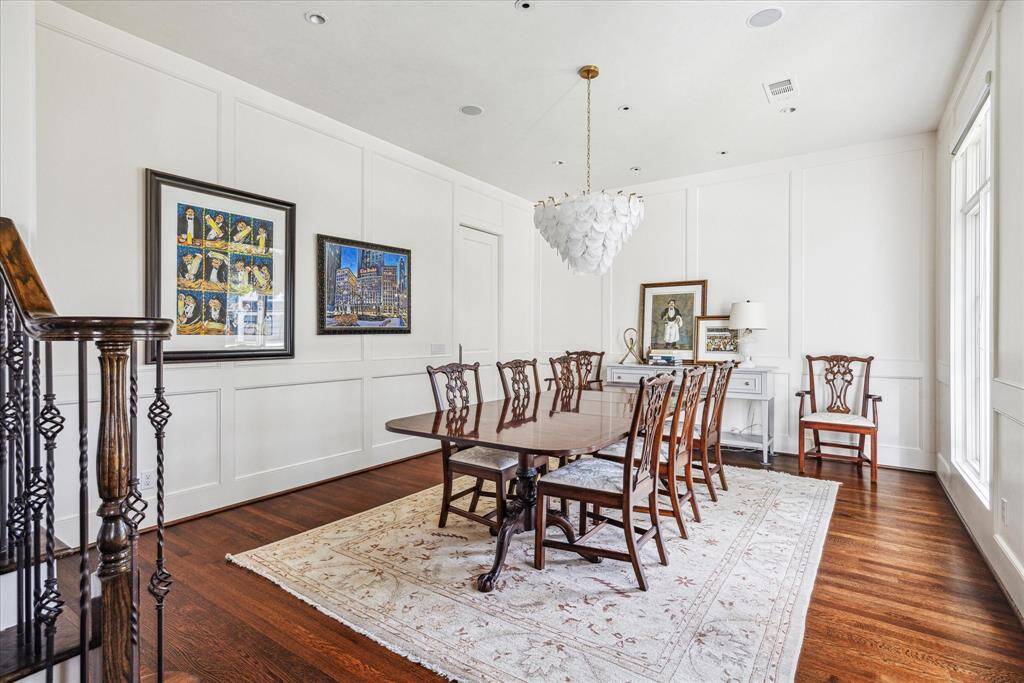 The formal dining room exudes timeless elegance with rich hardwood flooring, custom wall paneling, and an airy layout perfect for entertaining. A sculptural chandelier adds a modern touch, while large windows flood the space with natural light.
