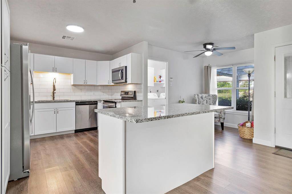 A modern kitchen with white cabinetry, stainless steel appliances, and a granite island with extension for seating.  Great for entertaining or a quick meal **403 E Lake Drive, Livingston, TX 77351**