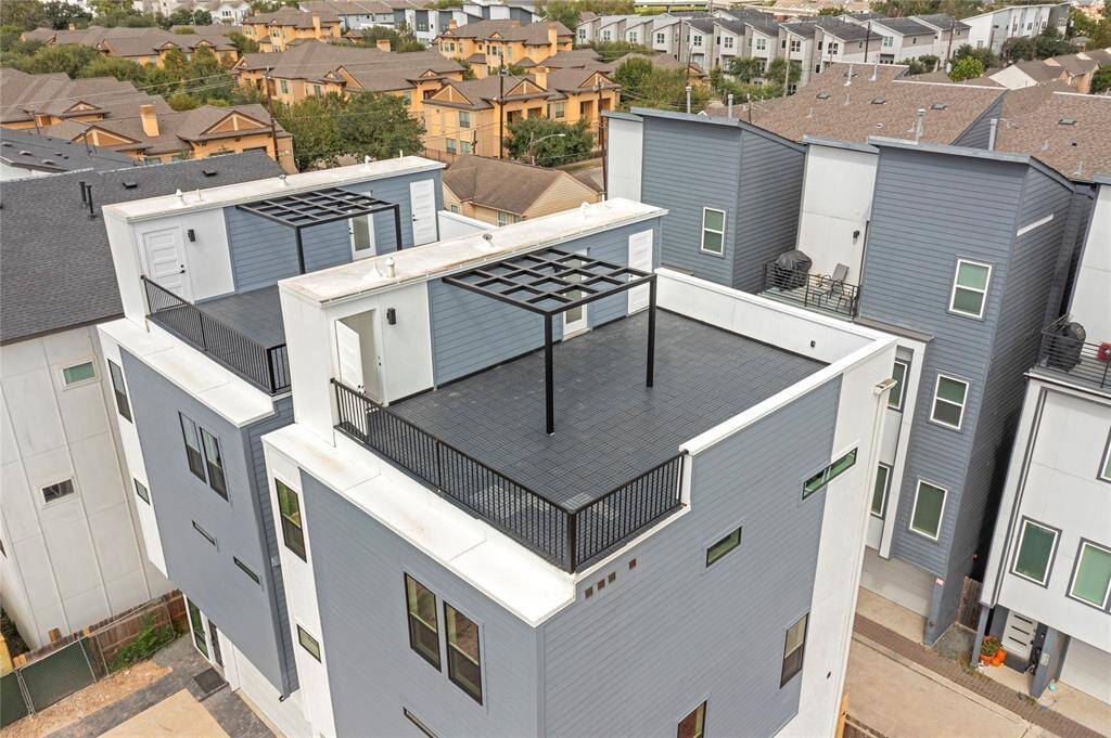 This is a bright and modern open-concept living space featuring hardwood floors, contemporary lighting fixtures, a built-in desk area or dry bar, and a staircase with metal railings. Large windows provide ample natural light.