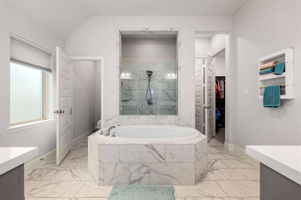 This primary bathroom is definitely move-in ready! Featuring a walk-in shower with tile surround, separate garden tub for soaking after a long day with custom tile detailing, dark stained cabinets with light countertops, spacious walk-in closet with shelving, high ceilings, neutral paint, sleek and modern finishes.