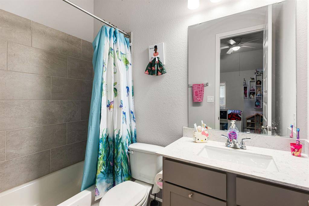 Secondary bathroom features light countertops and dark cabinets, neutral paint, shower/tub combo with tile surround, large mirror, tile floors and plenty of space to accommodate any visiting family or guests.