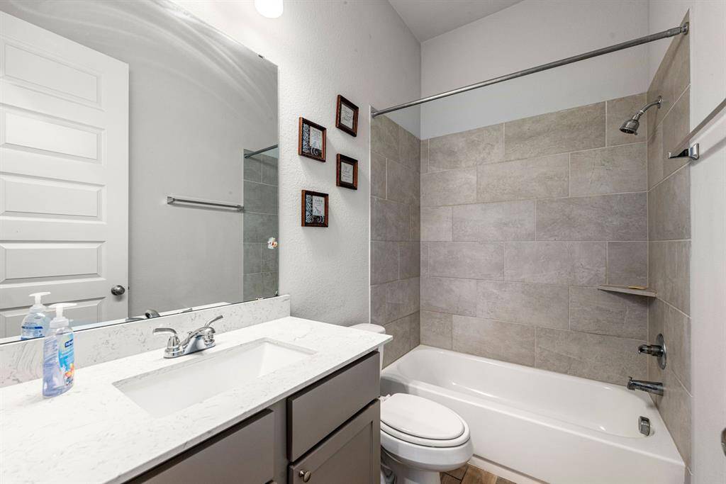 Secondary bathroom features light countertops and dark cabinets, neutral paint, shower/tub combo with tile surround, large mirror, tile floors and plenty of space to accommodate any visiting family or guests.