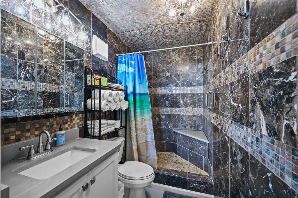 he updated bathroom features a striking dark tile design, quartz countertop, and a rock-tile walk-in shower with a built-in seat. Modern fixtures and thoughtful lighting add both elegance and comfort.