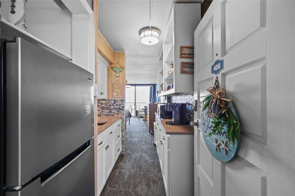 Step inside to a bright, welcoming space featuring updated cabinetry, quartz countertops, stainless-steel appliances, and stylish backsplash. The open layout draws your eye through the cozy living area to the balcony with ocean views beyond.