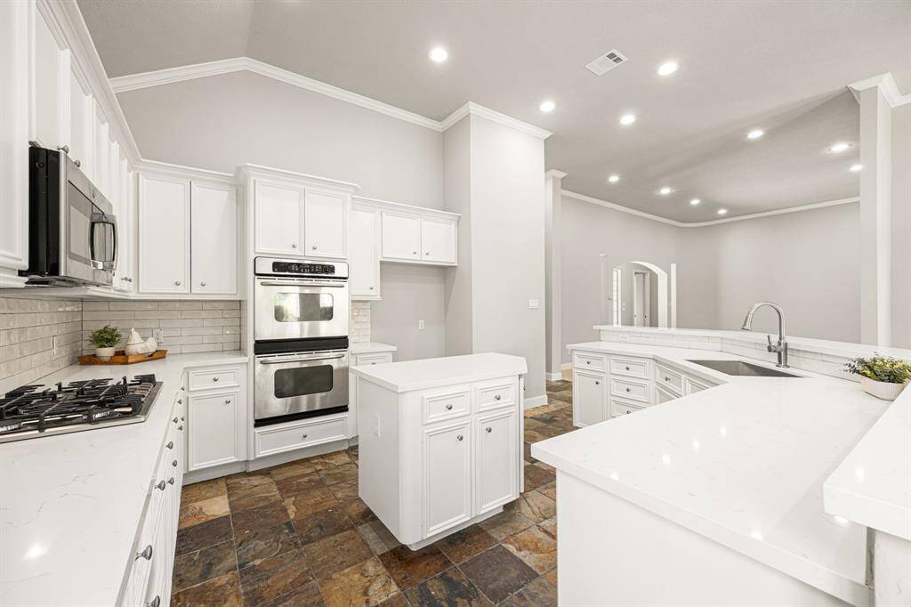 The Kitchen features stainless steel appliances, including GE double ovens, a newly installed 5-burner gas cooktop with a microwave above, and ample cabinet and counter space, along with a convenient center island with additional storage.