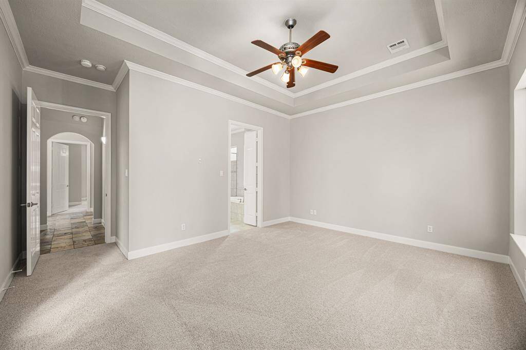 The Primary Suite offers plenty of space for various furniture arrangements, allowing for flexible and functional design. You can also see the entrance to the Primary Bath through double doors, along with the hallway that leads to another Bedroom and a Full Bath. The room also features a ceiling fan for added comfort.