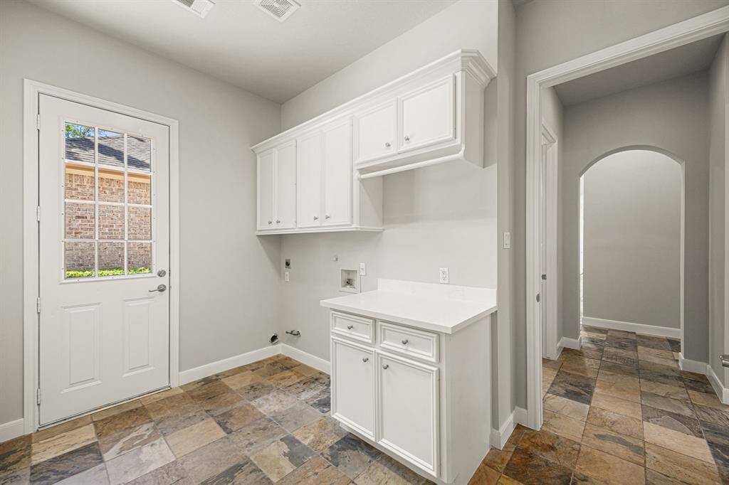 The Laundry Room is spacious, featuring cabinets above for storage, a quartz countertop, slate flooring, and a door leading to the driveway and garage, and a gas connection for a gas dryer.