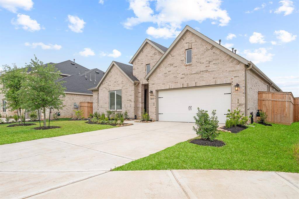 Welcome Home! A modern, single-story brick home with a two-car garage, neatly landscaped front yard, and a spacious driveway. The property features a wooden fence for added privacy and is set against a clear blue sky.