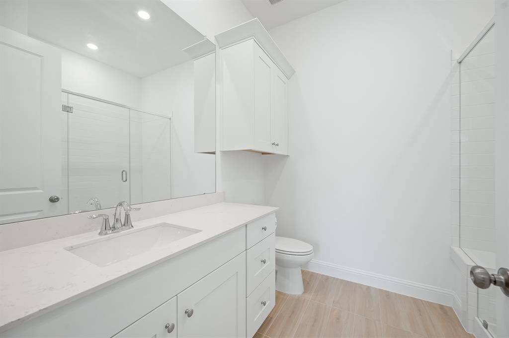 Next Gen® Suite bathroom features a modern design with white cabinetry, a sleek countertop, and a spacious glass-enclosed shower. The light wood flooring adds warmth to the bright, clean space.