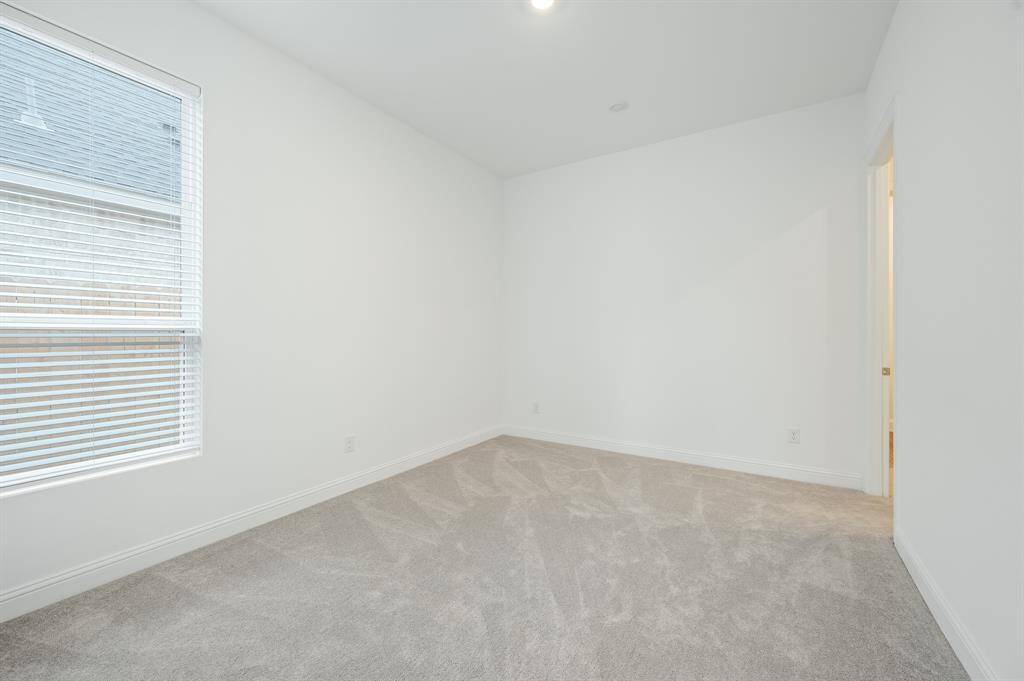 Next Gen® Suite bedroom with neutral-toned carpet and walls. It features a large window with blinds, allowing natural light to fill the space
