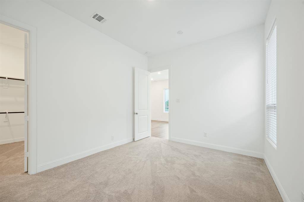 This is a bright, carpeted Next Gen® Suite bedroom with neutral walls. It features a walk-in closet, a window offering natural light