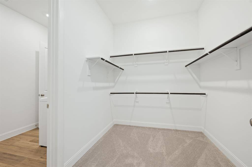 This is a spacious walk-in closet in the Next Gen® Suite with white walls, carpeted flooring, and multiple shelves and hanging rods for ample storage.