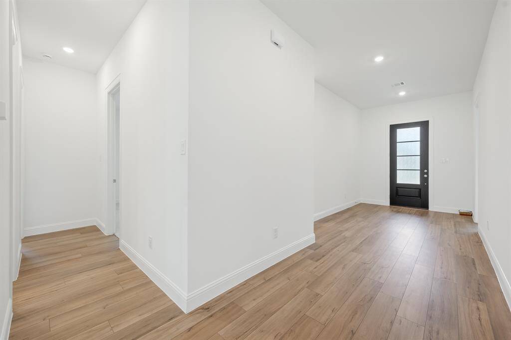 Bright, modern entryway with light wood flooring, white walls, and recessed lighting. Features a stylish black front door with frosted glass panels, creating a welcoming atmosphere.