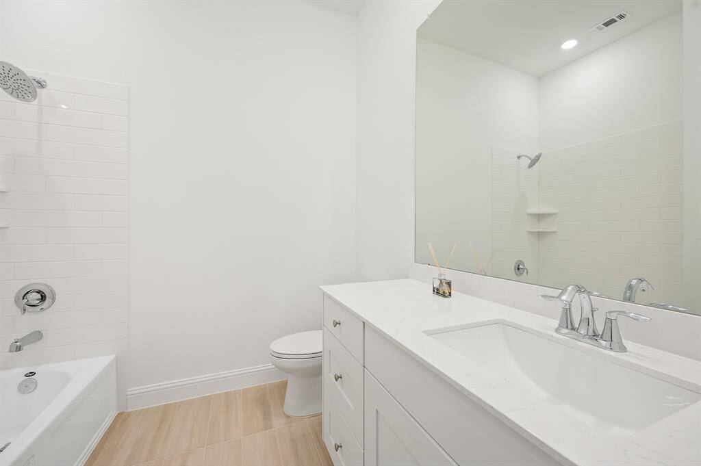 This secondary bathroom features a clean and modern design with a white color palette. It includes a bathtub with a shower head, a sleek vanity with a large mirror, and a polished sink, creating a bright and inviting space.