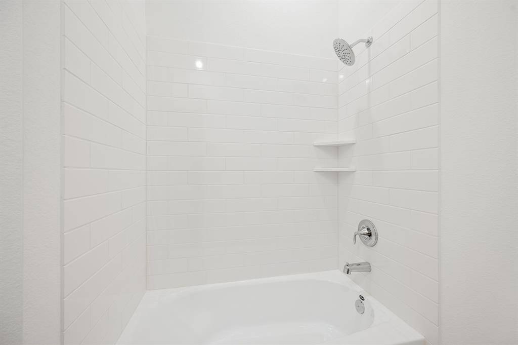 A modern bathroom with white subway tile walls, a bathtub, and a sleek chrome shower-head.