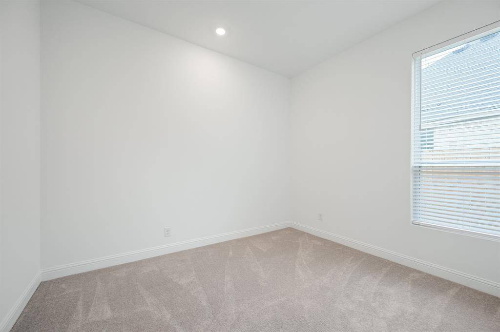 Secondary bedroom with white walls, a single recessed ceiling light, carpet flooring, and a window with blinds, offering natural light.