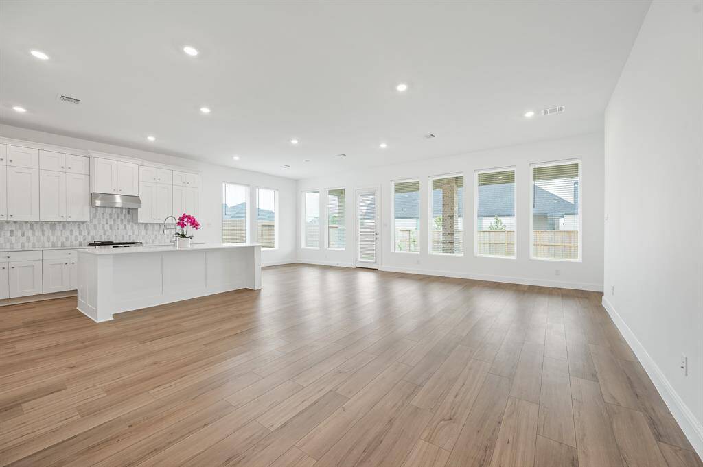 Spacious open-concept living area with abundant natural light, featuring a modern kitchen with white cabinetry, a large island, and wood flooring throughout.