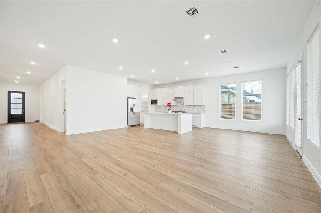 Bright and spacious open-concept living area with modern kitchen, featuring light wood flooring, white cabinets, and ample natural light from large windows.