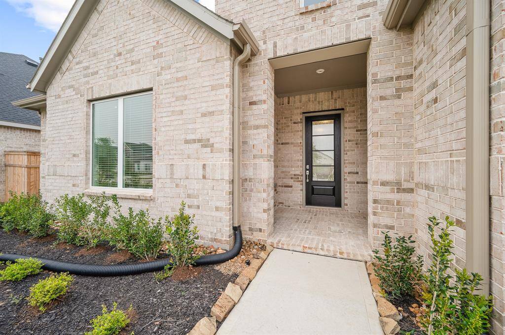 This photo showcases the entrance of a contemporary brick home, featuring a black front door with a sleek design. The pathway is bordered by well-maintained landscaping with small shrubs, giving it a welcoming and modern appeal.