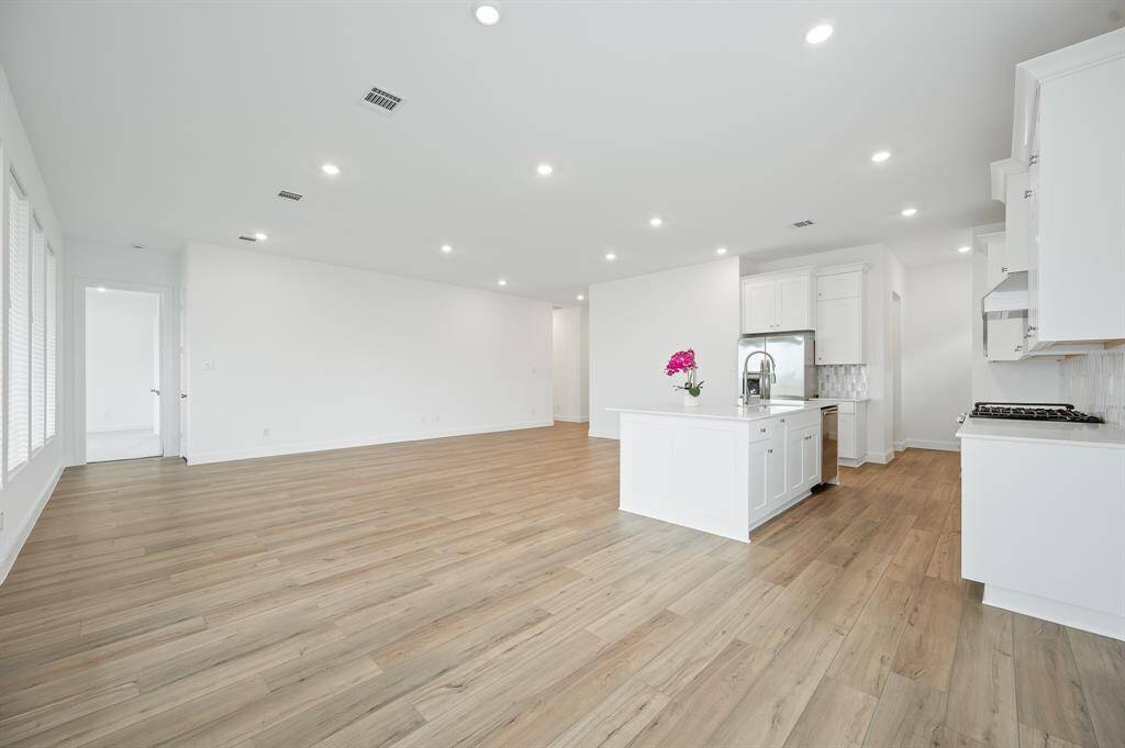 This spacious, open-concept living area features sleek wood flooring, recessed lighting, and a modern kitchen with white cabinetry and an island. It offers a bright, clean, and versatile space perfect for customization.