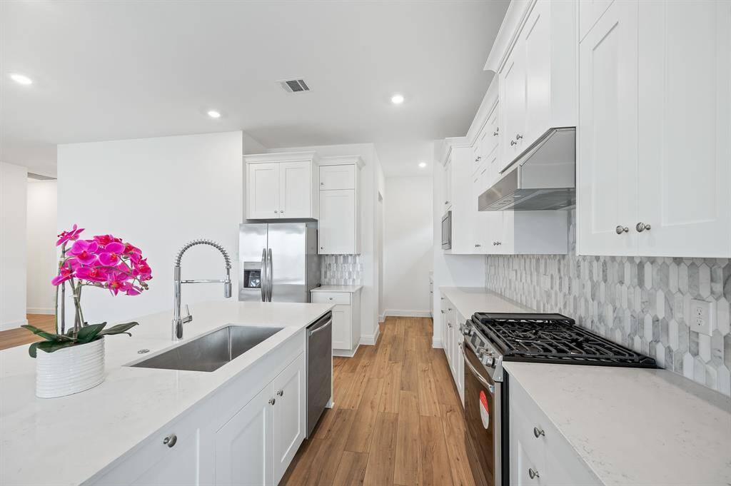This modern kitchen features sleek white cabinetry, stainless steel appliances, and a stylish hexagonal tile backsplash. The space is bright and inviting, with wood flooring and a center island with a sink and dishwasher.
