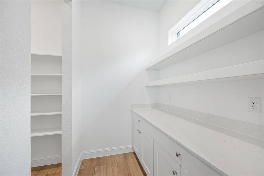 Bright and spacious pantry with ample shelving and counter space, featuring sleek white cabinetry and a small window for natural light. Perfect for organized storage.