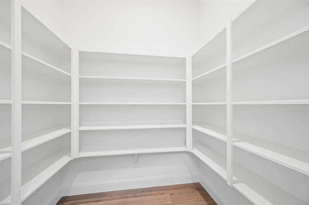 This photo shows a spacious walk-in pantry with white shelving on three walls, offering ample storage space. The light walls and wood style flooring create a bright and inviting atmosphere.