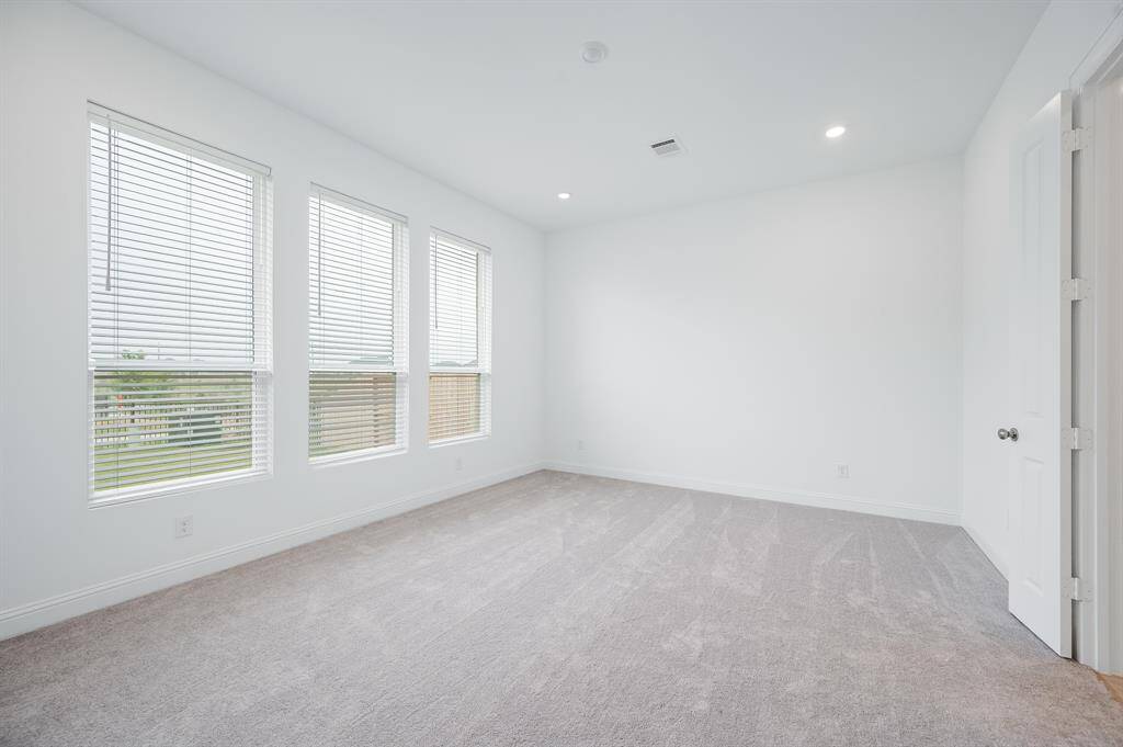 Bright and spacious primary bedroom with large windows, neutral walls, and soft carpeting.