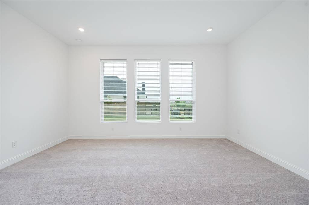 Spacious, bright primary bedroom with neutral carpet and three large windows, offering plenty of natural light.