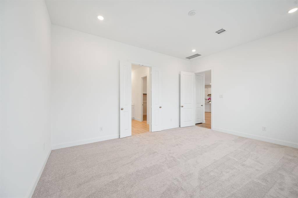 Spacious, bright primary bedroom room with neutral walls and carpet, featuring recessed lighting. It has two white doors leading to adjacent areas, highlighting a clean and modern design.