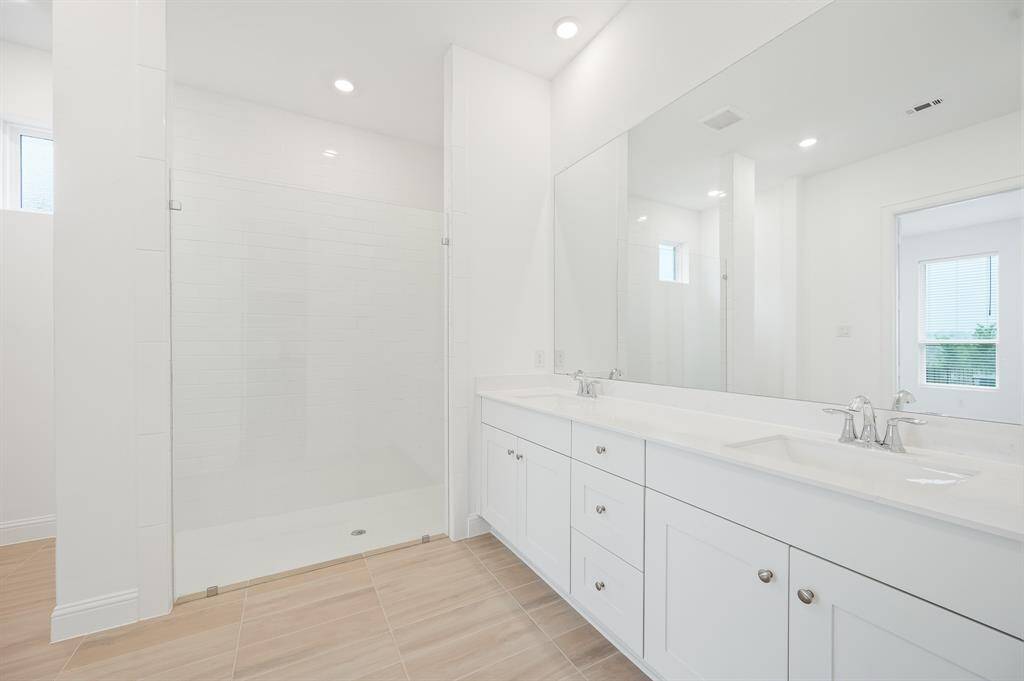 Primary bathroom features a spacious walk-in shower with a glass door, a large dual-sink vanity with ample storage, and sleek modern fixtures. The neutral color palette and large mirror create a bright, airy atmosphere.