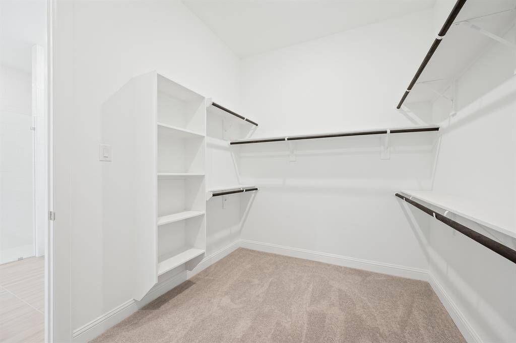 Spacious, primary walk-in closet with ample shelving and hanging space. The carpeted floor and white walls create a clean, bright atmosphere. Ideal for organized storage.