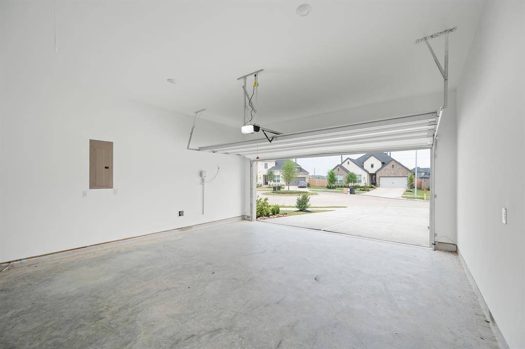 This photo shows a spacious, bright garage with a clean concrete floor and an open door revealing a view of a quiet residential street. Ideal for parking or additional storage.