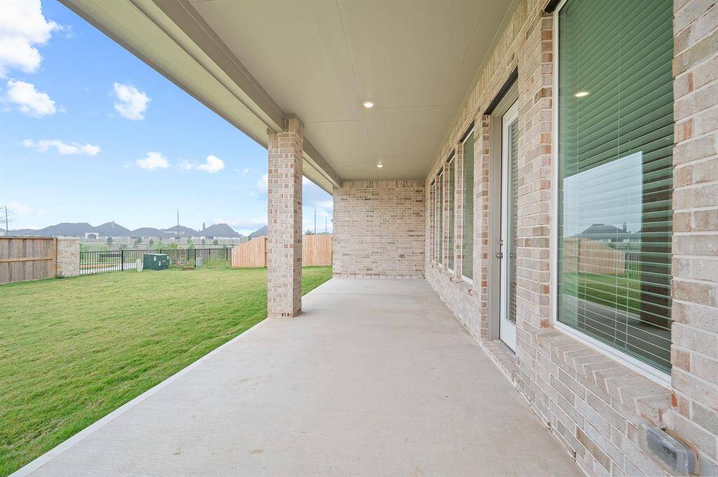 This photo showcases a spacious covered patio with brick accents and large windows, overlooking a well-maintained fenced backyard, ideal for outdoor relaxation and entertainment.