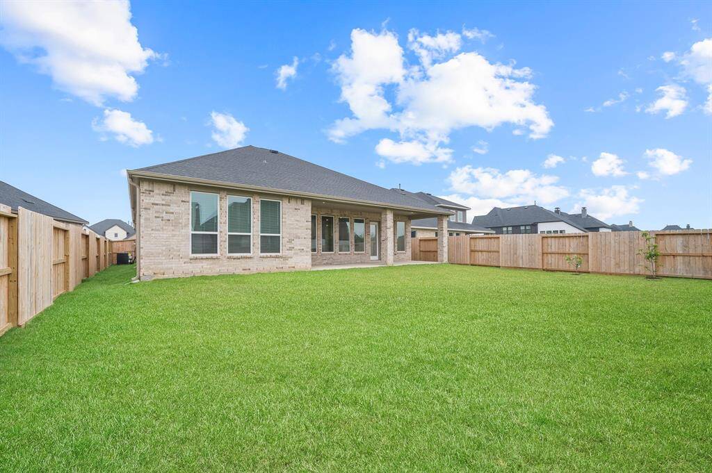 This photo showcases a spacious backyard with a well-maintained lawn, bordered by a wooden fence for privacy. The back of the house features large windows and a covered patio area, ideal for outdoor relaxation and entertaining.