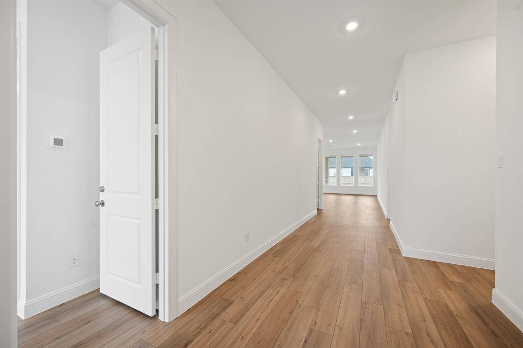 Bright and spacious hallway with wood flooring, recessed lighting, and a view of large windows at the end.