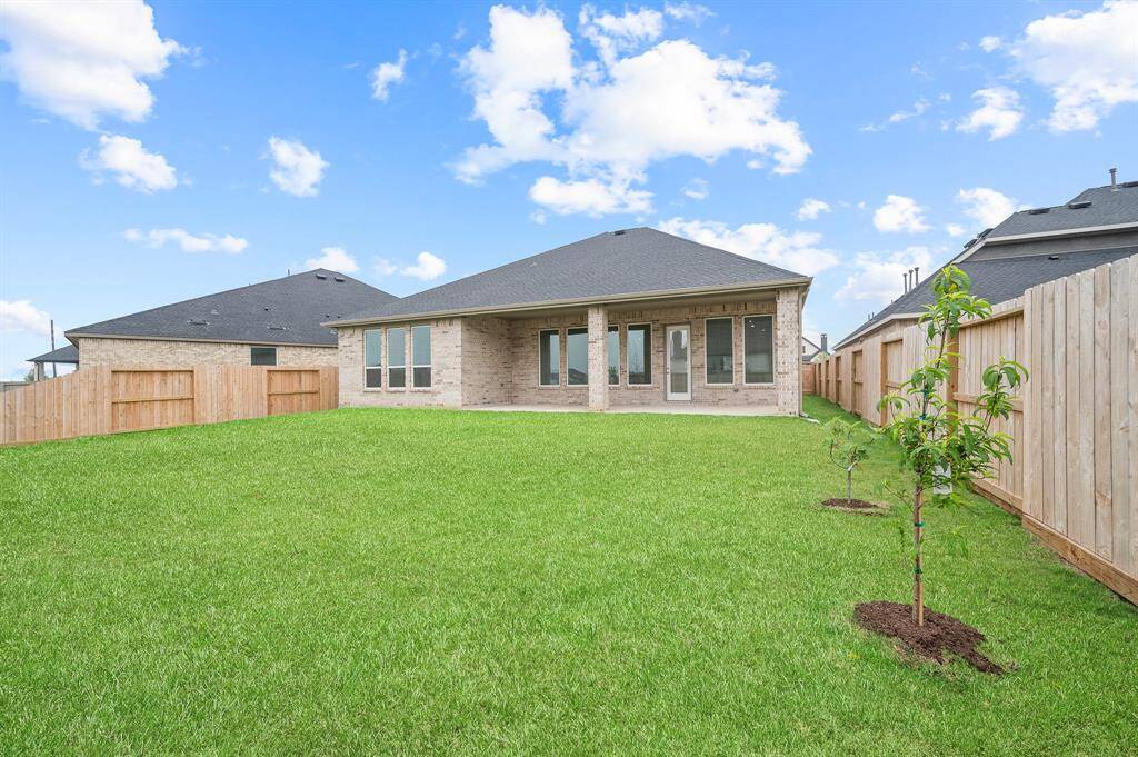 Spacious backyard with lush green lawn, bordered by wooden fencing for privacy. Features a covered patio area and young trees, ideal for outdoor activities and relaxation.
