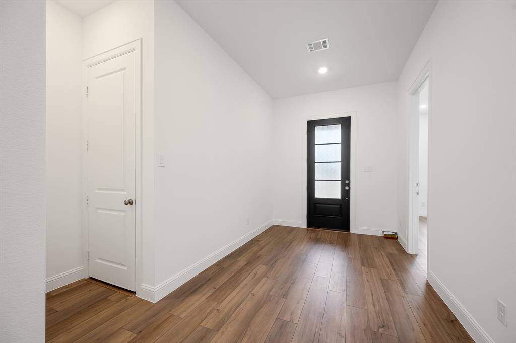 This entryway features a modern black door with frosted glass, white walls, and wood-look flooring, creating a bright and welcoming space.