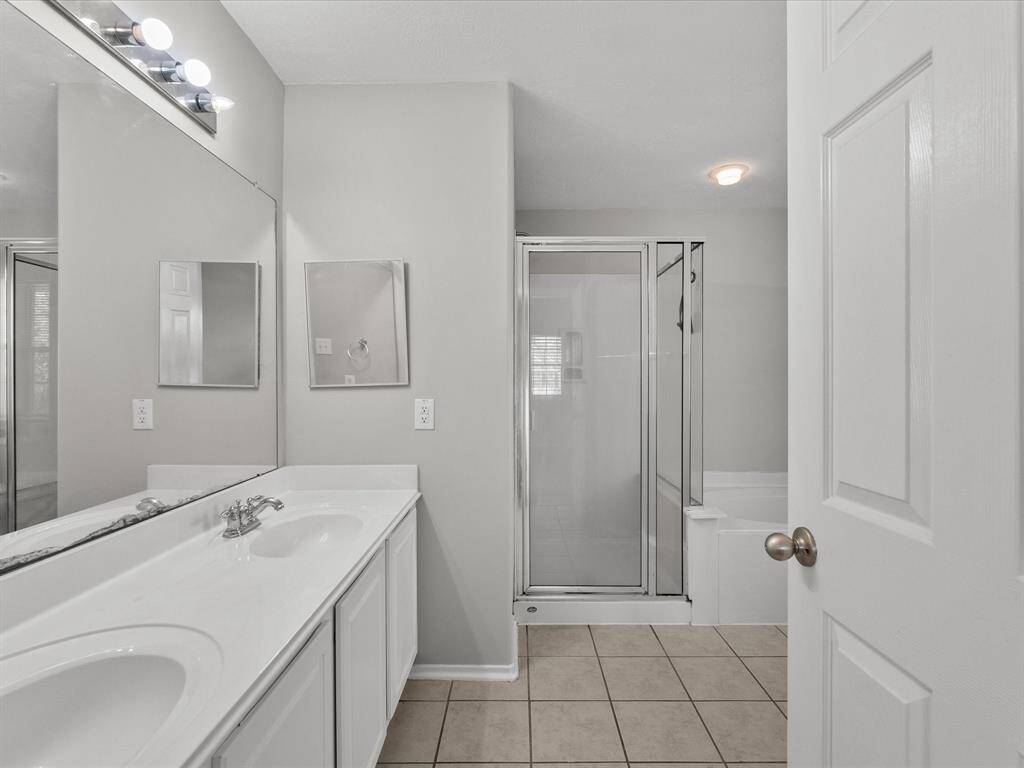 Primary bathroom features dual sinks, decor vanity and lighting, spa like tub w/glass shower