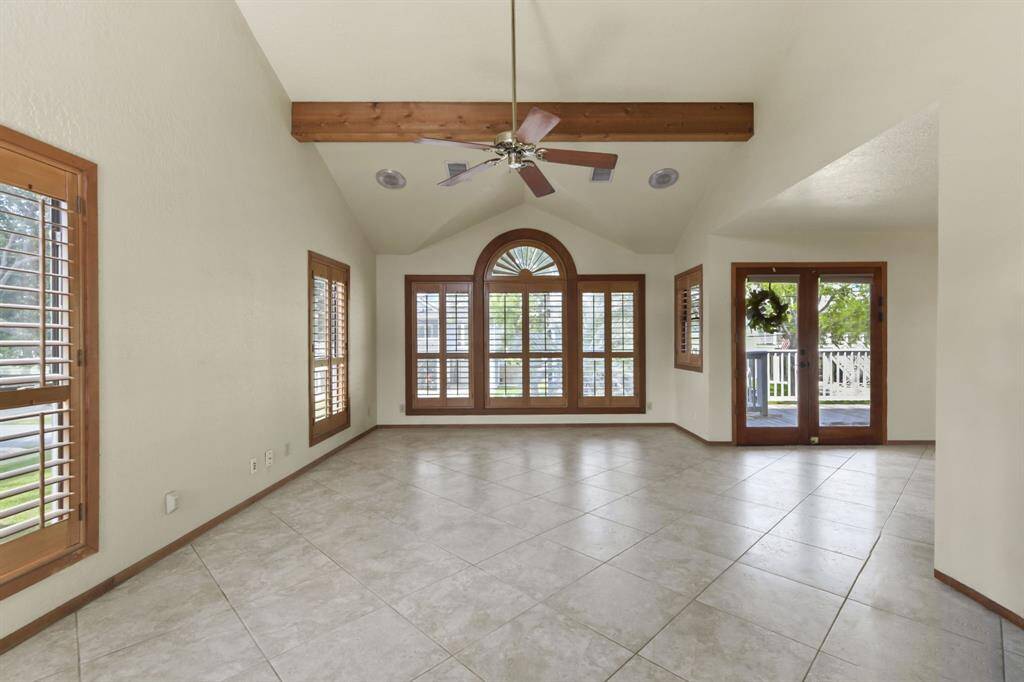 Bright and inviting space featuring high ceilings, exposed beams, and elegant tile flooring. Natural light pours in through large windows with classic shutters, offering a warm and welcoming atmosphere.