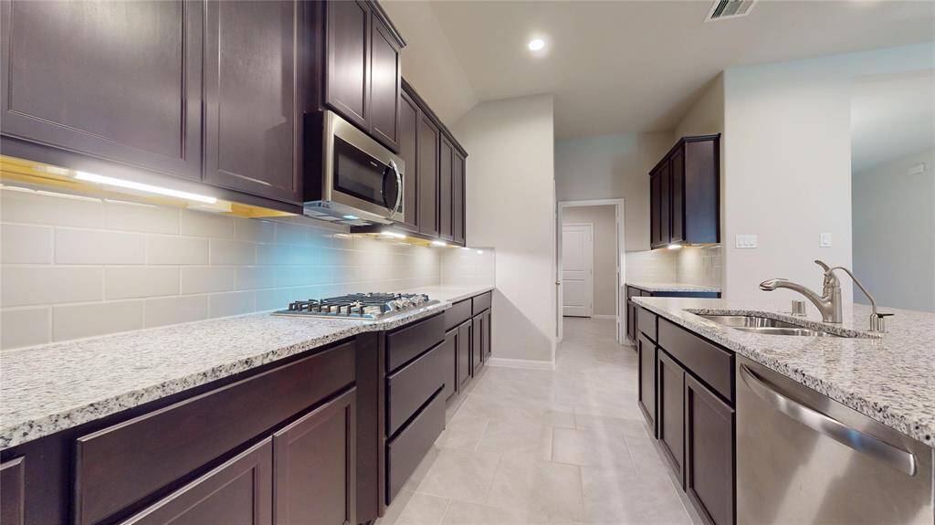 View from behind the island showcases the ample storage and work surfaces in this kitchen.  Granite countertops and glass subway tile backsplash.  All stainless appliances.  Gas cooktop, built-in microwave and double oven.