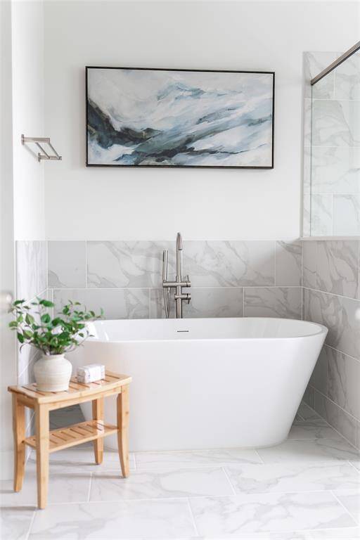 Luxurious primary bath featuring a sleek, modern design with a freestanding tub, elegant marble tile, and soothing artwork for a spa-like retreat.