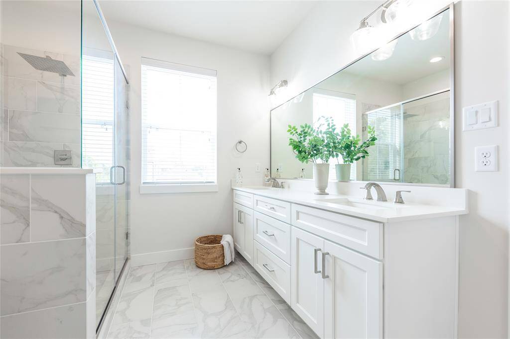 Luxurious primary bath featuring elegant marble finishes, a spacious glass-enclosed shower, and a double vanity with ample storage.