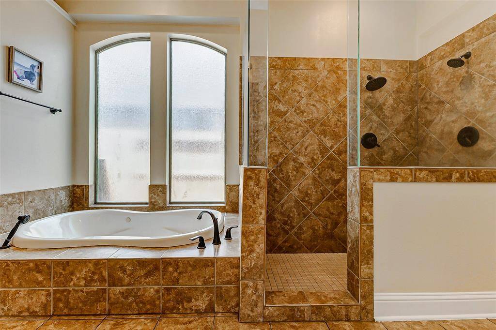 The primary bathroom is both spacious and well-appointed, offering double sinks, a jetted tub for relaxing baths, and a separate full-entry shower for added convenience. Designed with soft brown and white natural tones, the space feels calm, inviting, and beautifully balanced — a perfect place to start and end your day.