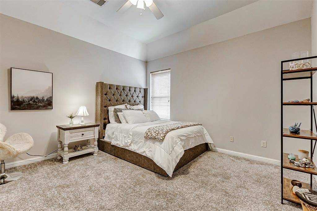 This bedroom pairs classic design elements with modern comfort, featuring neutral-toned carpeting that complements any décor. A large window provides ample daylight, while a ceiling fan adds a finishing touch to this well-appointed space. Its generous size allows for versatile furniture arrangements.