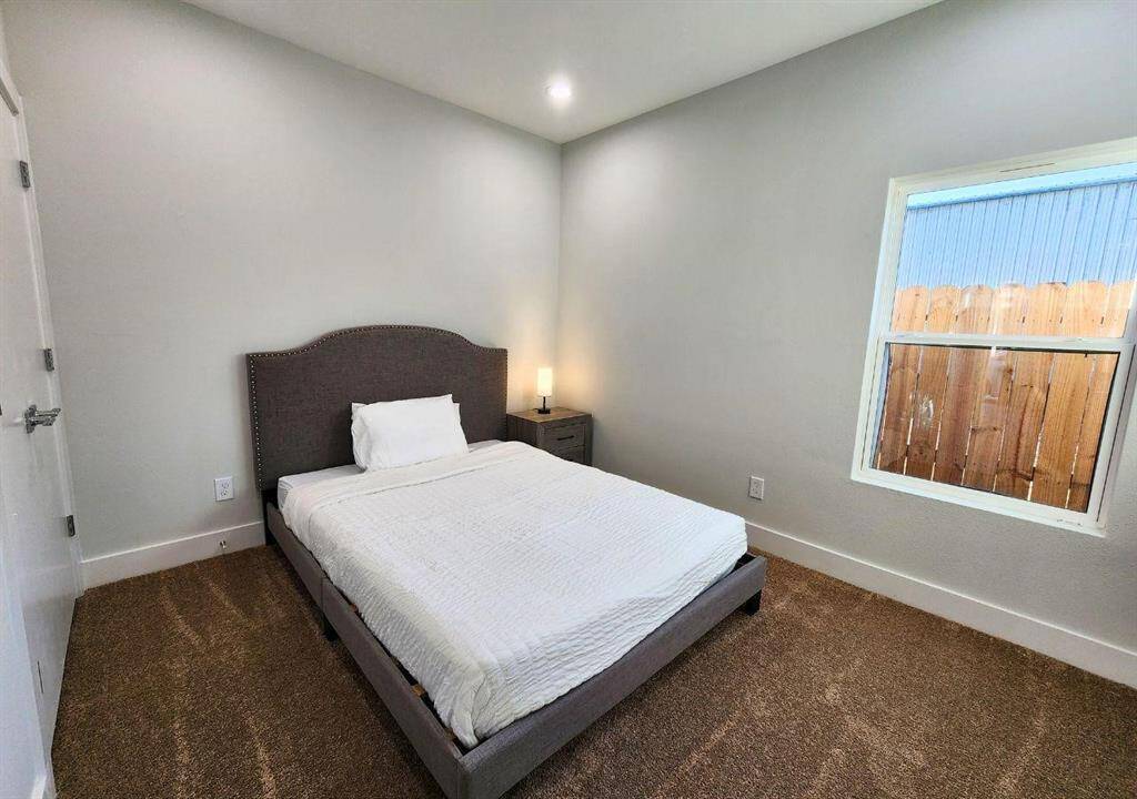 Cozy bedroom with a simple, modern design. Features a window allowing natural light to enter. The room has carpeted flooring and light walls, creating a warm atmosphere.