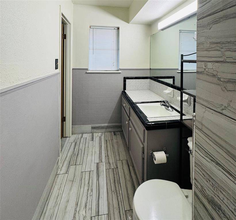 This bathroom features a full-entry shower with stylish gray tiles, complemented by a spacious vanity with a sink and black tiled accents. A large mirror adds the finishing touch, creating a clean look