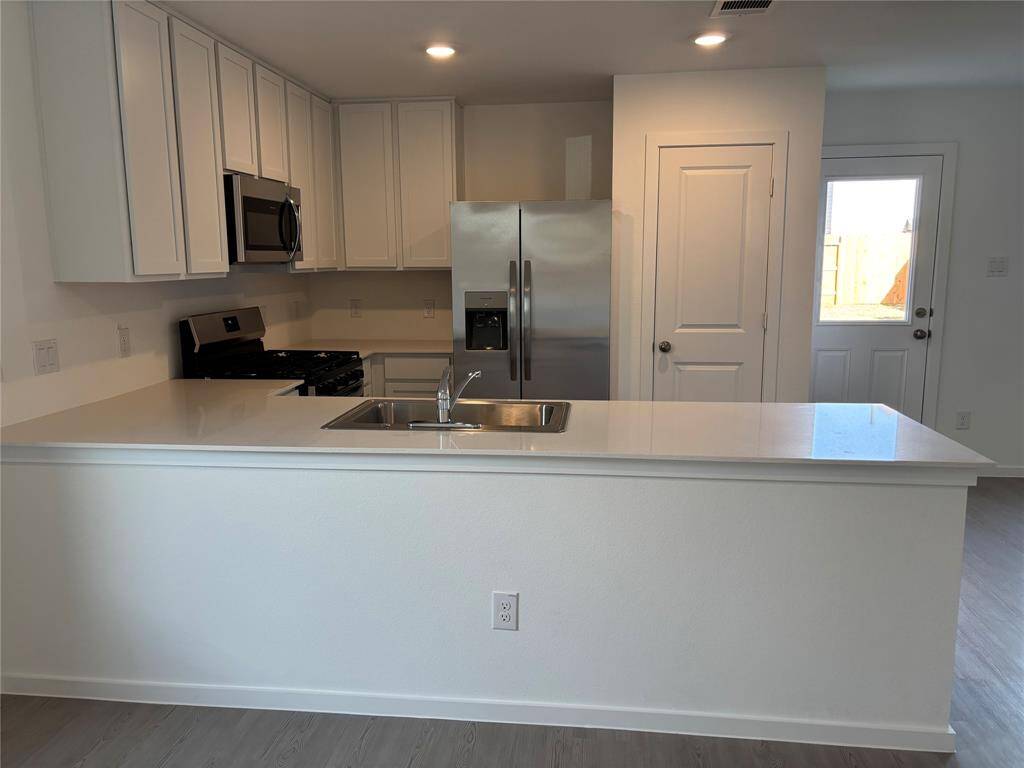 Modern kitchen with sleek white cabinetry, stainless steel appliances, and a spacious island with a sink. Bright and inviting, featuring recessed lighting and access to the backyard.