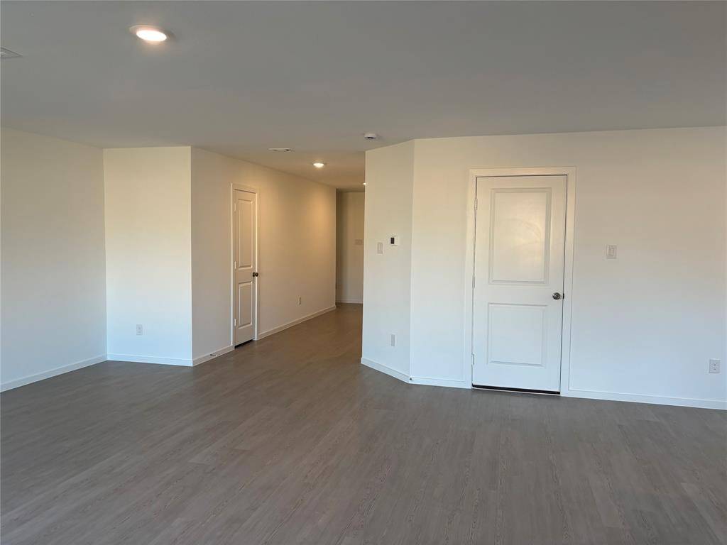 This photo shows a spacious, open room with wood-look flooring and neutral-colored walls. It features recessed lighting and two white doors, creating a clean and modern feel.